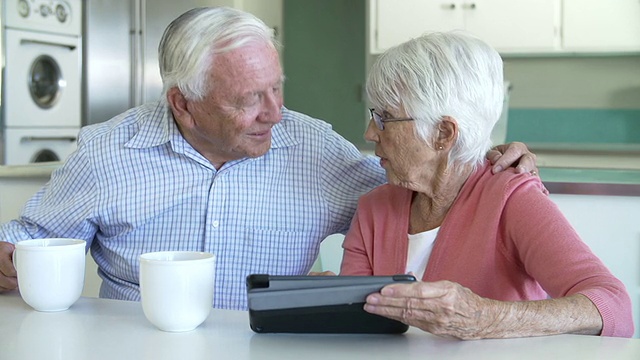 一对老年夫妇坐在餐桌前使用平板电脑视频素材