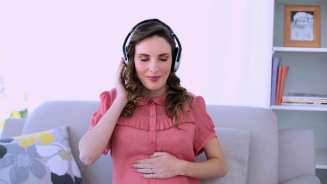 漂亮的怀孕模特坐在沙发上听音乐视频素材