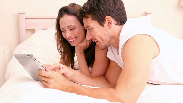 幸福的夫妇躺在床上用平板电脑视频素材