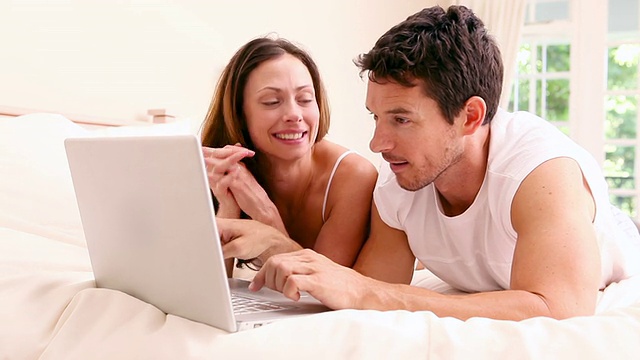 幸福的夫妇躺在床上一起使用笔记本电脑视频素材