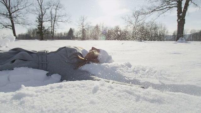 慢动作:快乐的女人躺下，做雪天使视频素材