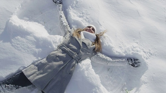 慢镜头:快乐的女人在阳光明媚的日子里做雪天使视频素材