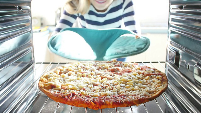 一个女人把意大利辣香肠披萨放进烤箱煮视频素材