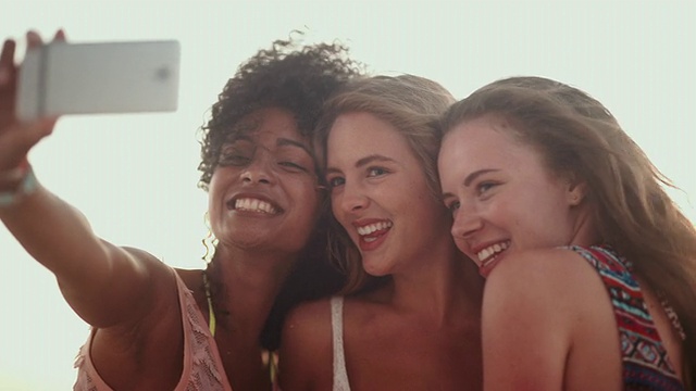 一群不同种族的朋友在海滩上用手机自拍，一边大笑一边做鬼脸视频素材