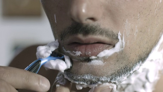 一个年轻男子用刀片剃须刀刮脸的特写视频下载