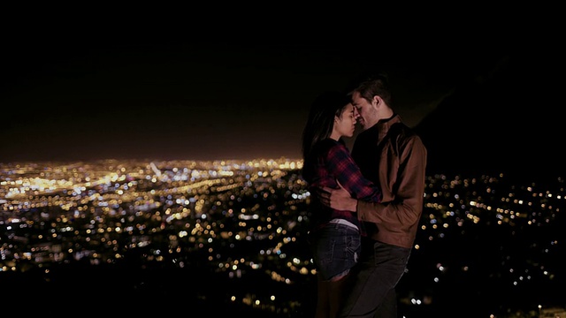 年轻的情侣在夜晚拥抱着身后的城市视频素材