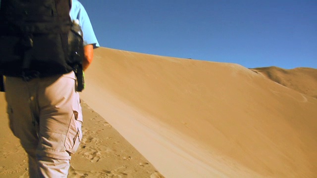 两个徒步旅行者攀登沙丘的顶部。视频下载