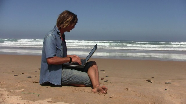 一个年轻人在海滩上用笔记本电脑工作视频下载