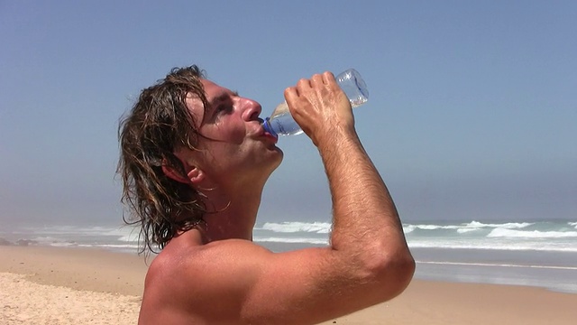 口渴的年轻人在海滩上喝水视频素材