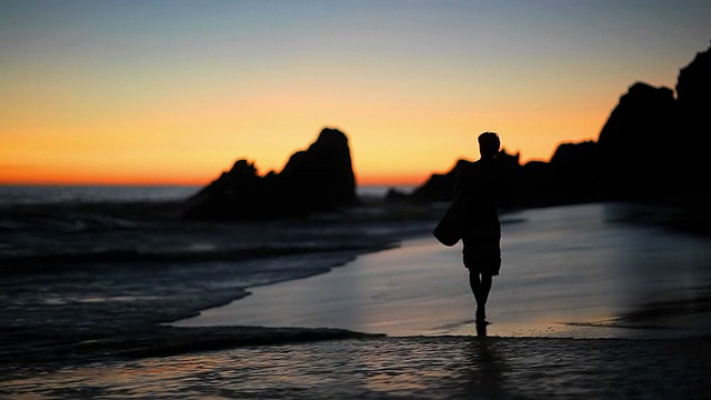 一个冲浪者沿着海滩行走的剪影视频素材