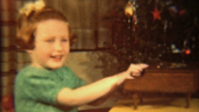 女孩在圣诞树旁弹奏玩具钢琴(1942复古8毫米)视频素材