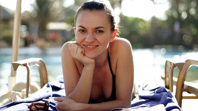 年轻微笑的女人躺在游泳池的日光浴床上视频素材