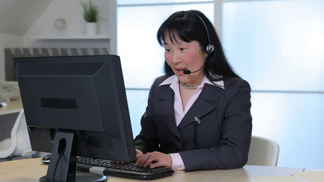 商务女性在办公室里通过耳机与电脑交谈视频素材
