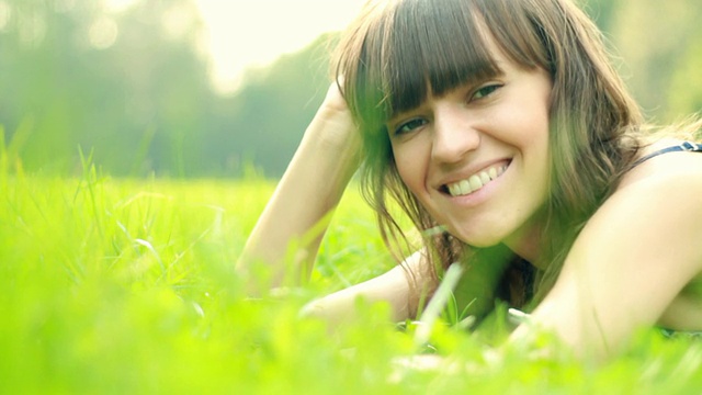 年轻幸福美丽的女人躺在草地上的肖像视频素材