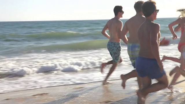 一群青少年朋友一起在海滩上跑步视频素材