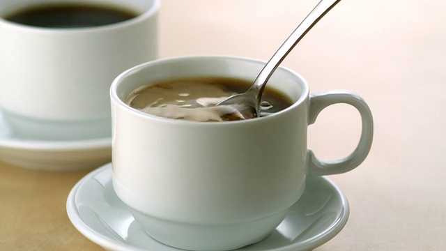 在咖啡中倒入牛奶并搅拌，慢动作视频素材