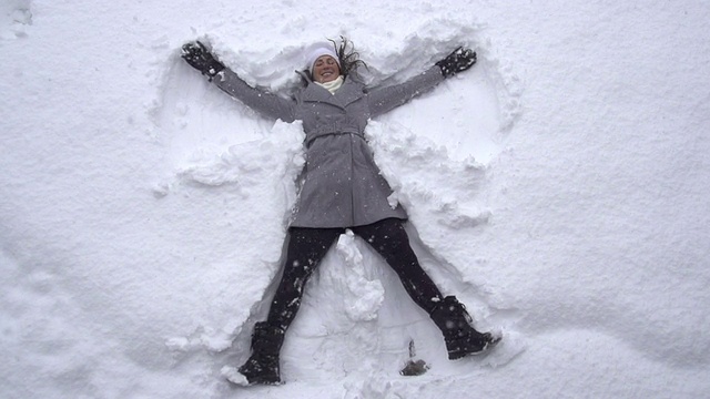 慢镜头:年轻女子在堆雪天使视频素材