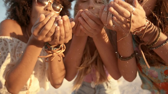 在慢镜头中，女孩们在海滩上用手吹五彩纸屑视频下载