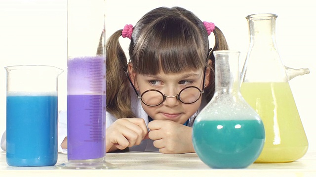 可爱的小女孩梳着两个马尾辫，穿着制服，圆眼镜站在白色背景的化学试管中间微笑着视频下载