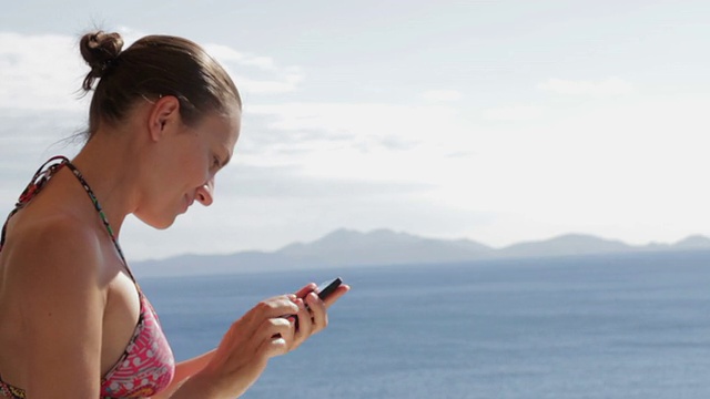 年轻女子在海滩上用手机拍照视频下载