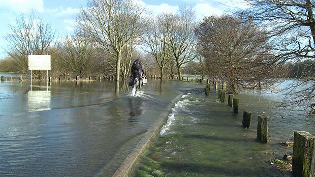骑自行车的人经过一条被洪水淹没的道路视频下载