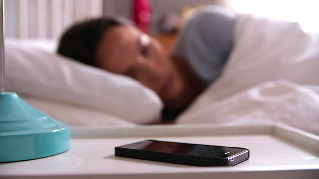 被手机闹钟吵醒的女人在床上看短信视频素材