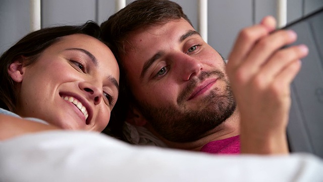 一对年轻夫妇用平板电脑躺在床上视频素材