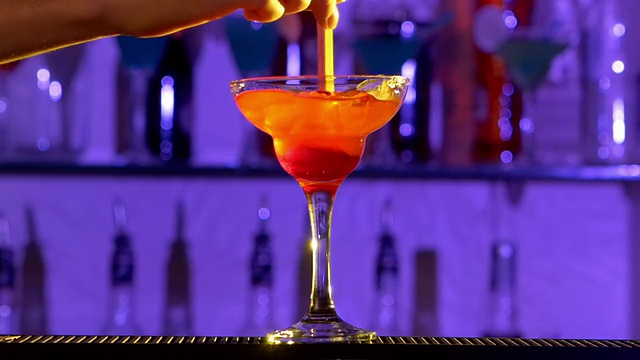 调酒师准备鸡尾酒用冰和两种透明液体，甜糖浆，在不寻常的玻璃杯中，慢动作，由小管混合，酒吧视频下载