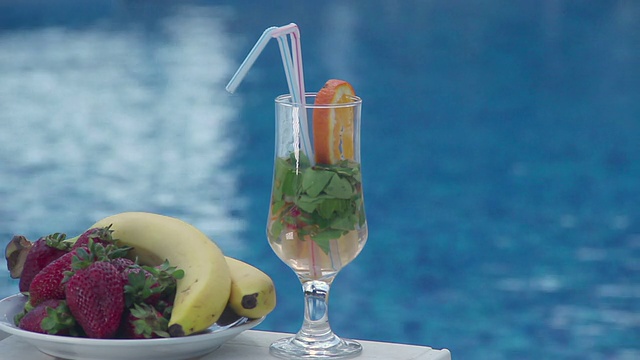 鸡尾酒和水果靠近游泳池，蓝色的水背景视频素材