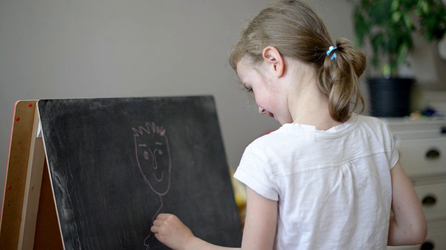 小女孩在黑板上画鬼脸。视频素材