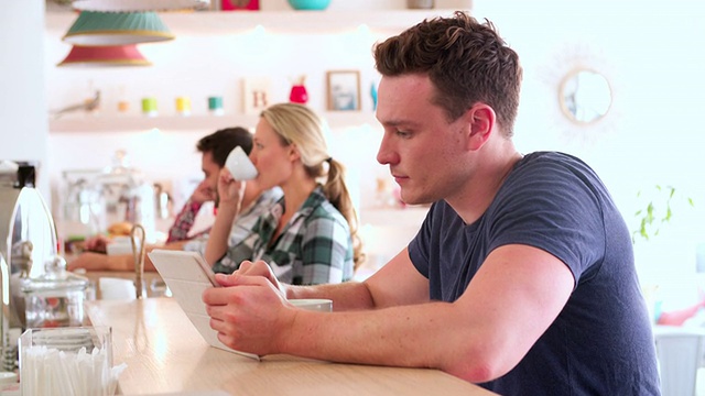 一个年轻人坐在咖啡馆里用着平板电脑视频素材