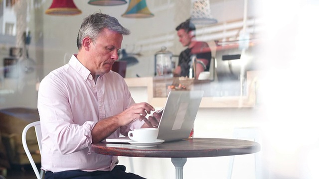 一个商人在一个咖啡馆的桌子上用笔记本电脑打电话视频素材