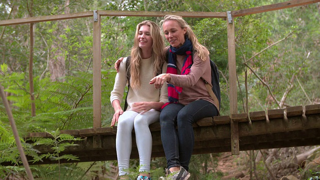 母女俩坐在森林里的一座小桥上视频素材