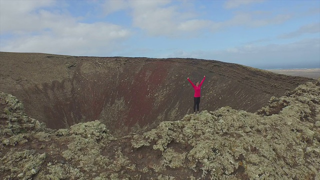 AERIAL:年轻女子在火山口顶端举起手臂视频下载