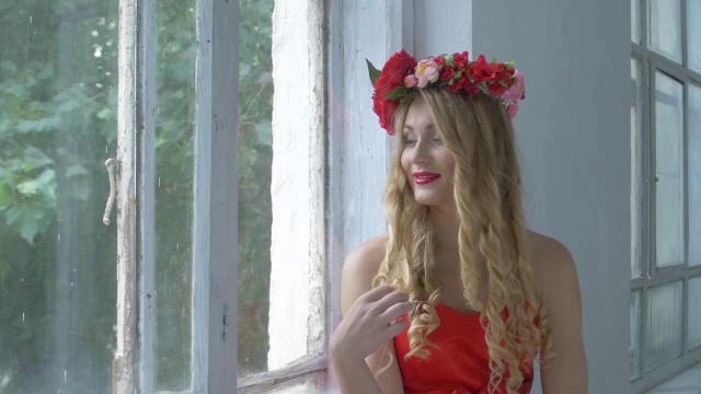 头戴红花花环的漂亮少妇坐在窗台上，面带微笑，慢镜头视频下载