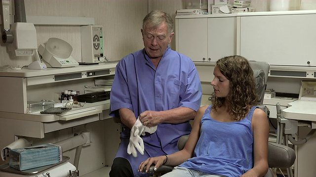 牙医在她的病人旁边戴上手套视频素材