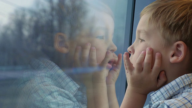 男孩用手捂着脸看着窗外视频素材
