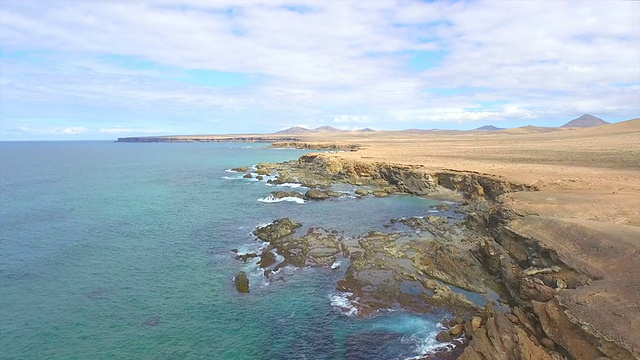 航拍:波涛汹涌的海洋上方的大沙漠和火山峭壁视频下载