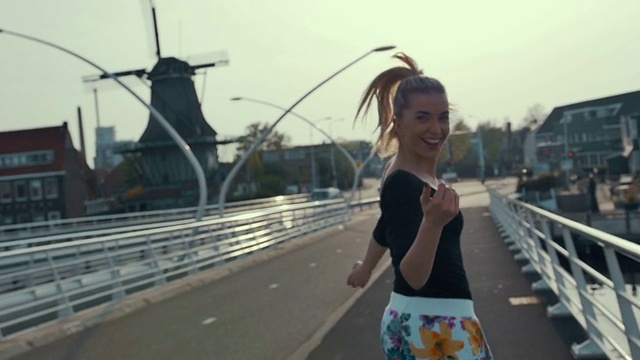 一个女性的剪影在夕阳下奔跑在荷兰的一座桥上，慢镜头。视频下载