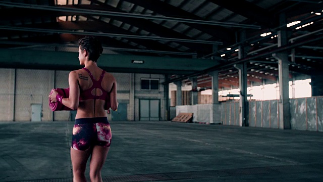 在工业健身房里，女人拿着粉红色的运动垫视频素材