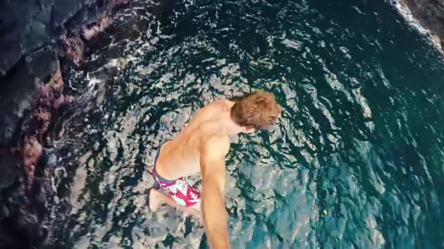 POV慢镜头年轻人从悬崖上跳到海里。极限悬崖跳有趣的夏季生活方式视频素材