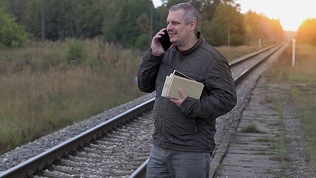 一个拿着智能手机和书在铁路附近行走的人视频下载