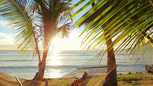 美丽的年轻女子放松在热带吊床在日落。视频素材