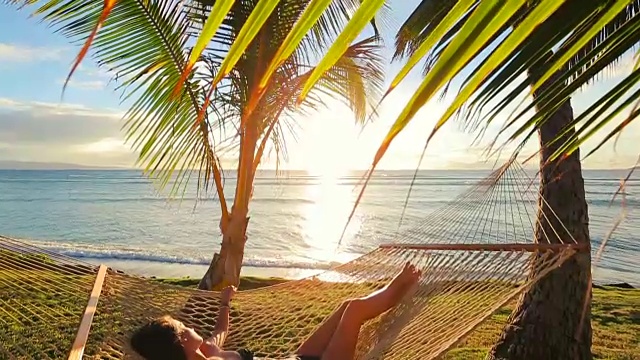 美丽的年轻女子放松在热带吊床在日落。视频素材