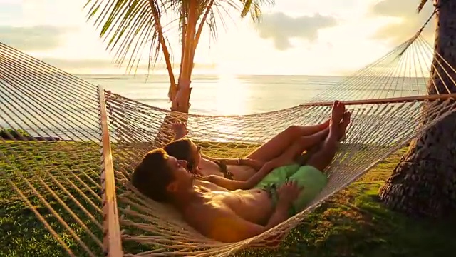 日落时分，浪漫的情侣在热带吊床上放松视频素材
