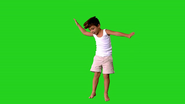 快乐的小男孩在绿色的屏幕上跳跃和旋转视频素材