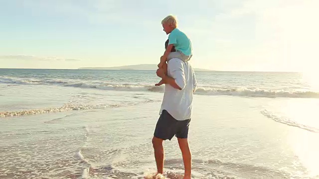 日落时分，父亲背着儿子在海滩上散步。视频素材