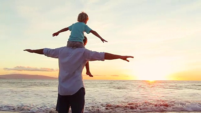 父亲和儿子在日落时分的海滩上一起玩飞机手臂游戏。视频素材