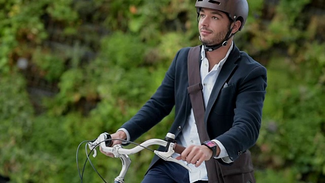 一名男子用平板电脑和智能手表在城市街道上骑自行车视频下载