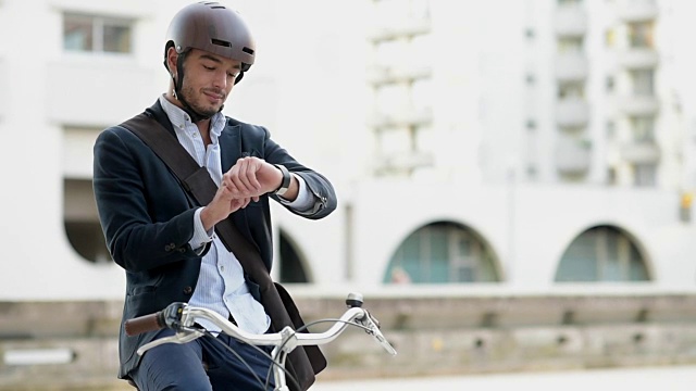 一名男子用平板电脑和智能手表在城市街道上骑自行车视频素材